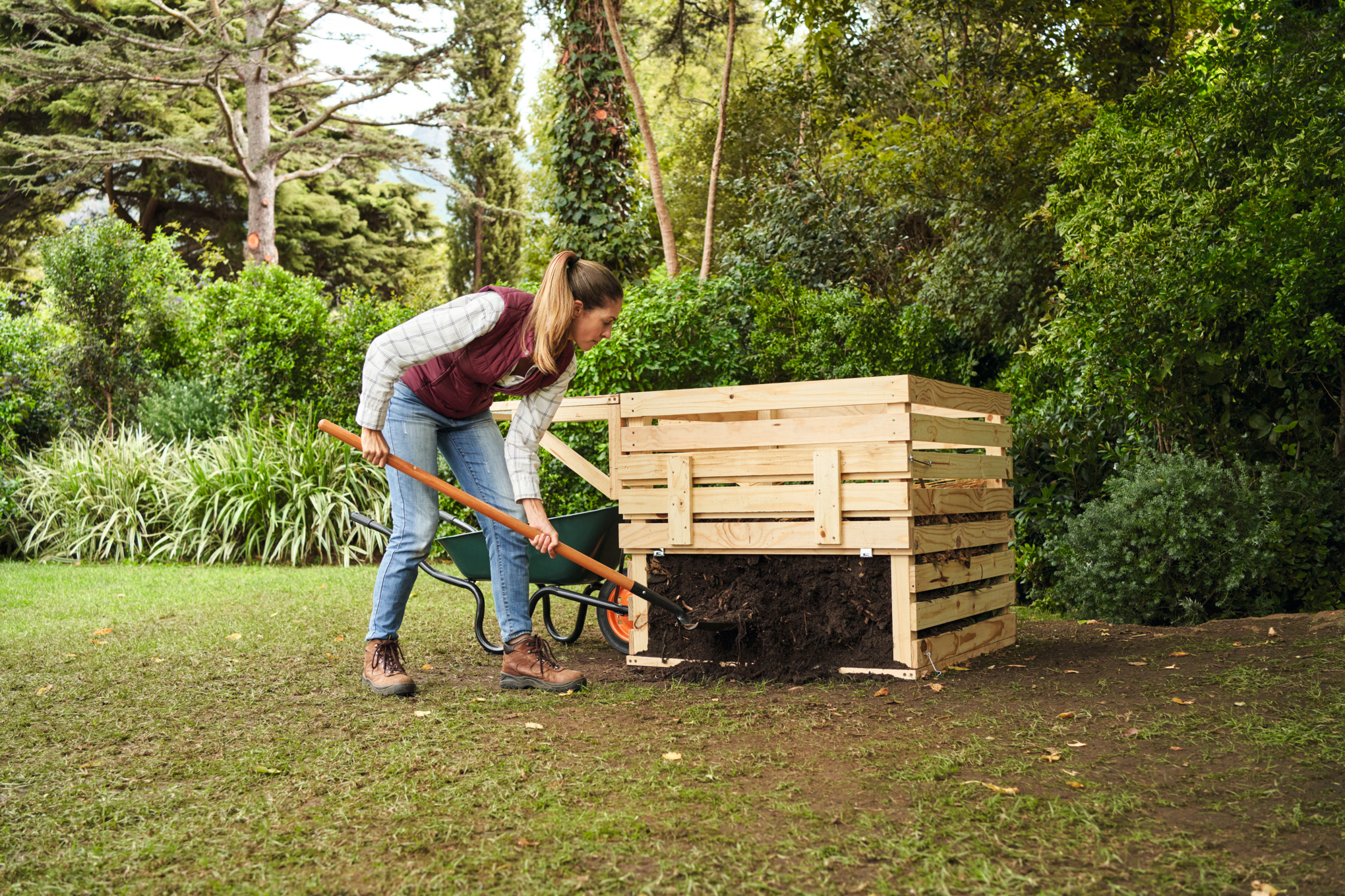 Une femme avec une queue de cheval mélange son compost avec une pelle